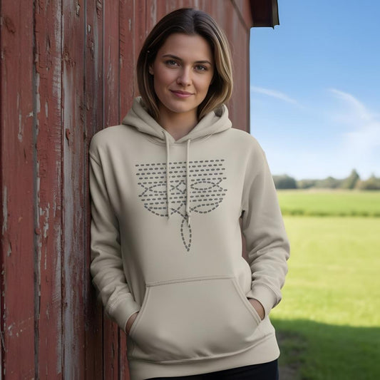Woman wearing a beige hoodie with a design, standing against a red barn door with a green field and blue sky in the background. Boot Stitch Hoodie for Horse Lovers, Barn Wear Equestrian Sweatshirt