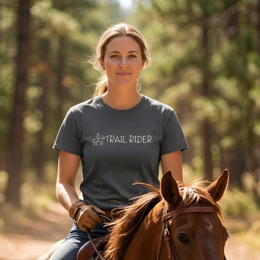 Woman riding a horse wearing a 'Trail Rider' t-shirt in a forest setting. Trail Rider T-Shirt for Horse Lovers, Equestrian Wear for Trail Riding