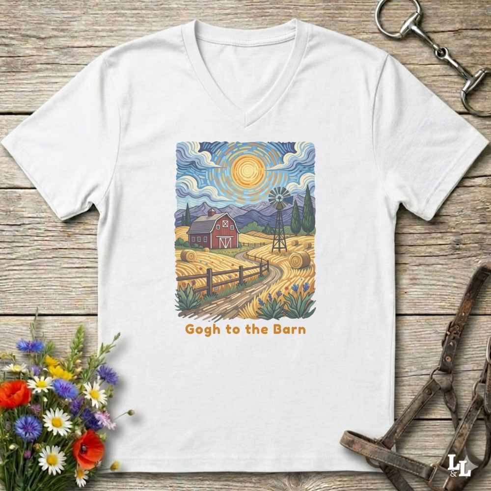 A white V-neck t-shirt laid flat on a rustic wooden surface, featuring a colorful Van Gogh-inspired barn scene graphic with the text 'Gogh to the Barn'. The shirt is styled with equestrian props (reins and a bit) and a small bouquet of wildflowers.