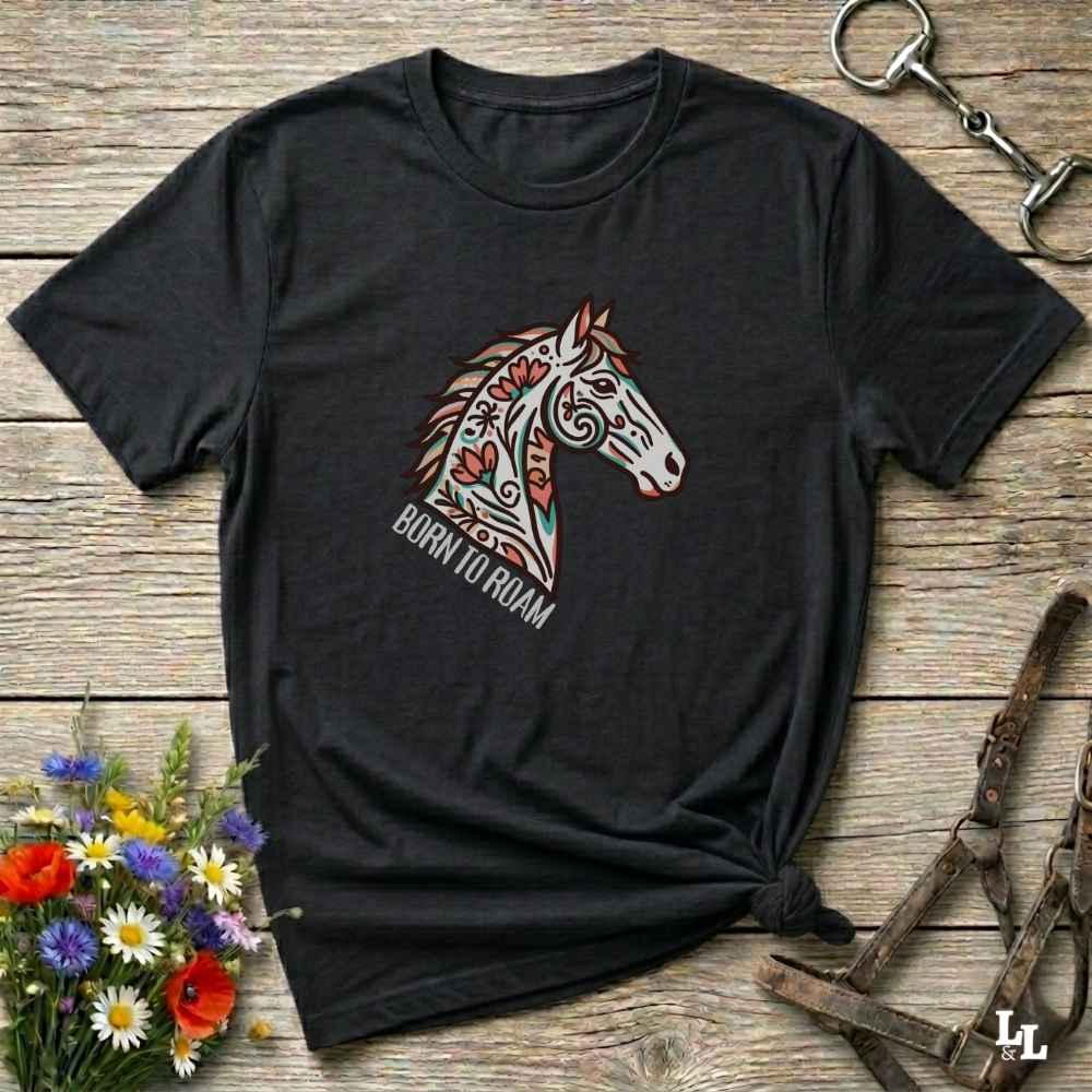 Black t-shirt with a colorful horse graphic and 'Born to Roam' text on a wooden surface with floral and equestrian-themed accessories.