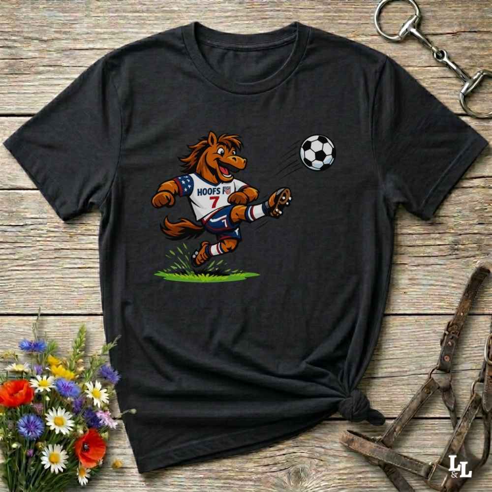 black t-shirt with a cartoon horse kicking a soccer ball on a wooden surface with flowers and horse halter and bit.