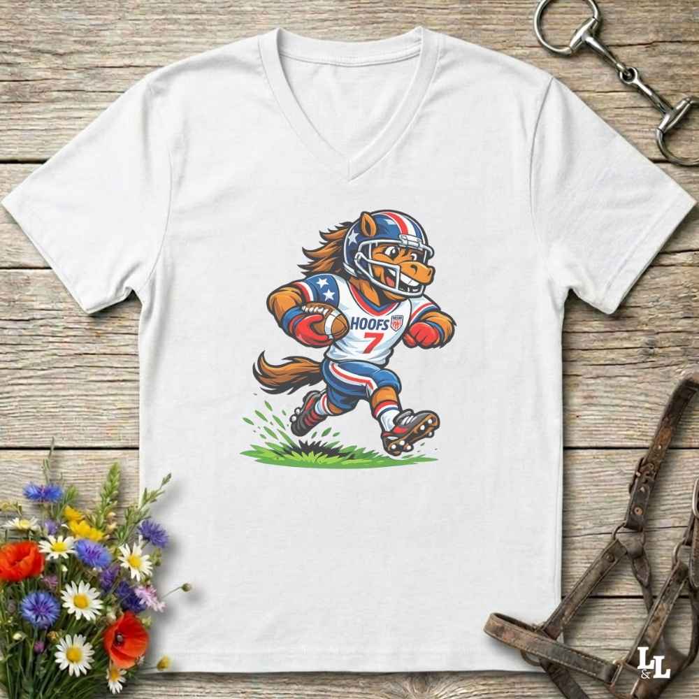 A white V-neck t-shirt laid flat on a rustic wooden surface, featuring a cartoon graphic of a horse mascot in a football uniform with the number 7. The shirt is styled with equestrian tack in the background and a small bouquet of flowers in the lower-left corner.