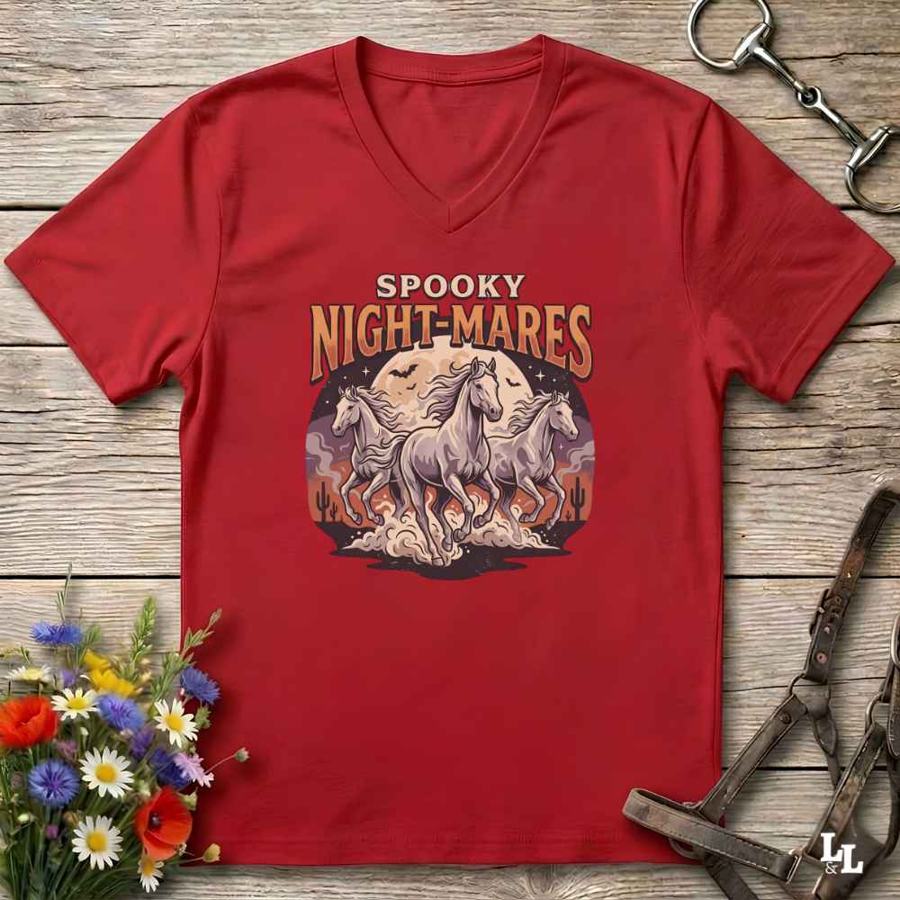 A red V-neck t-shirt with a 'Spooky Night-Mares' graphic print, laid flat on a rustic wooden background with horse tack and flowers as props.