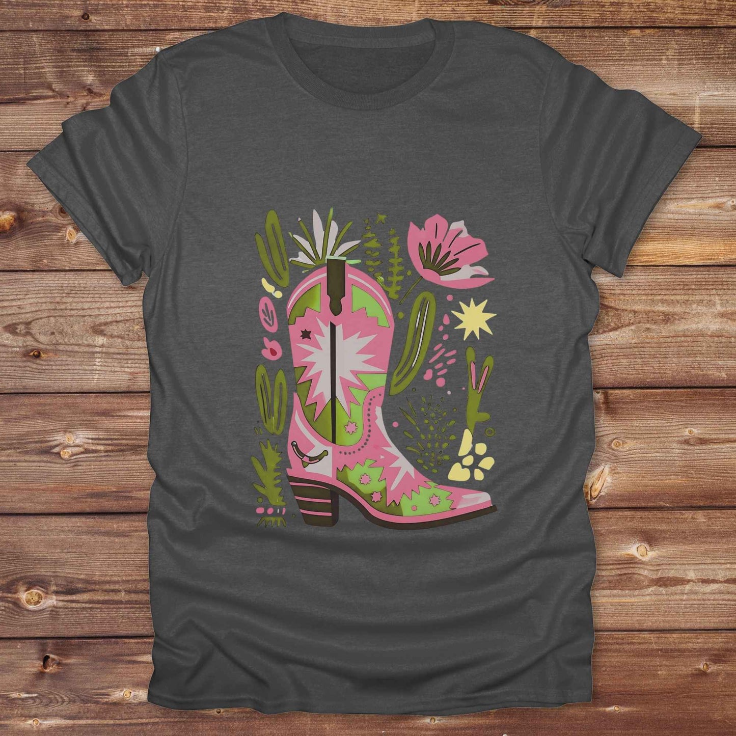 Bright pink and green cowgirl boot printed on a unisex western t-shirt, styled for a boho country vibe. The design is surrounded by floral and cactus illustrations to enhance the desert western theme.