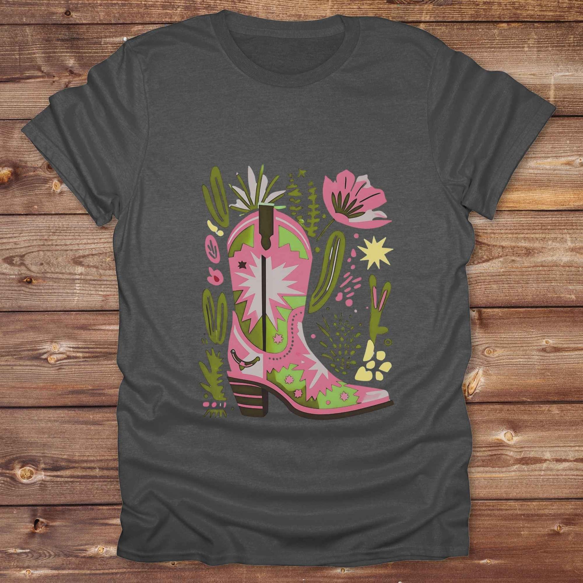 Bright pink and green cowgirl boot printed on a unisex western t-shirt, styled for a boho country vibe. The design is surrounded by floral and cactus illustrations to enhance the desert western theme.