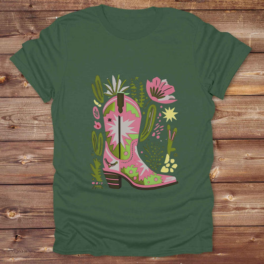 Bright pink and green cowgirl boot printed on a unisex western t-shirt, styled for a boho country vibe. The design is surrounded by floral and cactus illustrations to enhance the desert western theme.