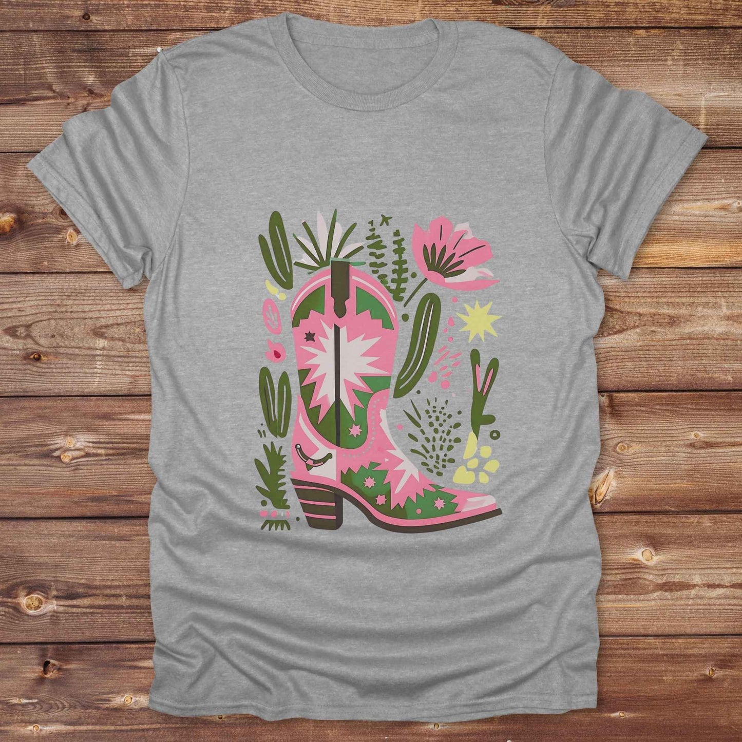 Bright pink and green cowgirl boot printed on a unisex western t-shirt, styled for a boho country vibe. The design is surrounded by floral and cactus illustrations to enhance the desert western theme.