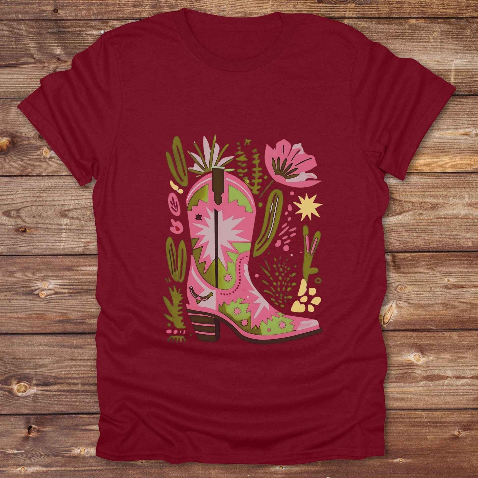 Bright pink and green cowgirl boot printed on a unisex western t-shirt, styled for a boho country vibe. The design is surrounded by floral and cactus illustrations to enhance the desert western theme.