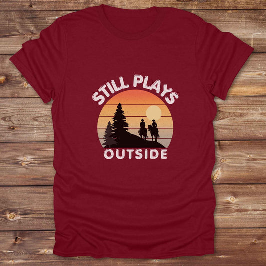 Still plays outside. Funny western t-shirt featuring horse-themed design for cowgirls, cowboys, and equestrians — perfect for rodeo lovers, rustic style fans, and horse people. Unique graphic tee by Lasso and Loom.