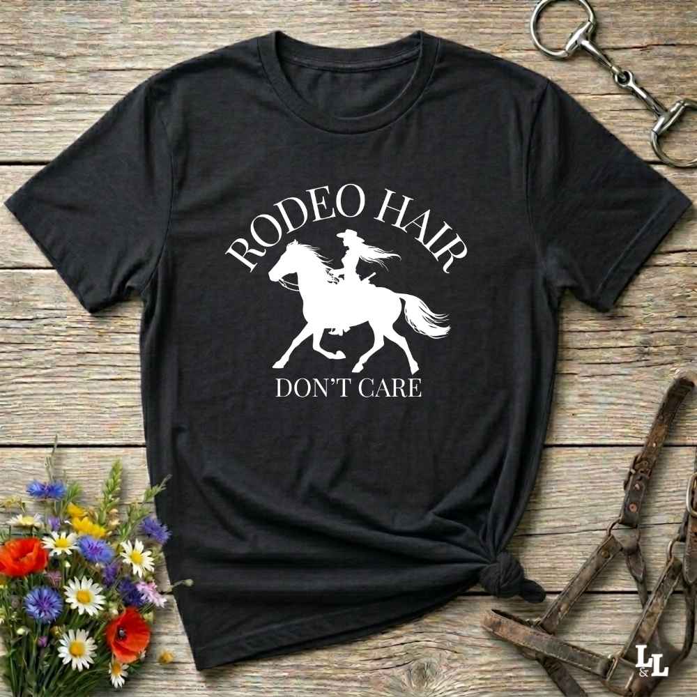typography cowgirl t-shirt styled for rodeo lovers and horse girls on rustic wooden background. Trendy cowgirl shirt designed for horse lovers, featuring bold western lettering in graphic style. Horse riding themed t-shirt with country slogan “Rodeo Hair Don’t Care” styled for modern cowgirls.