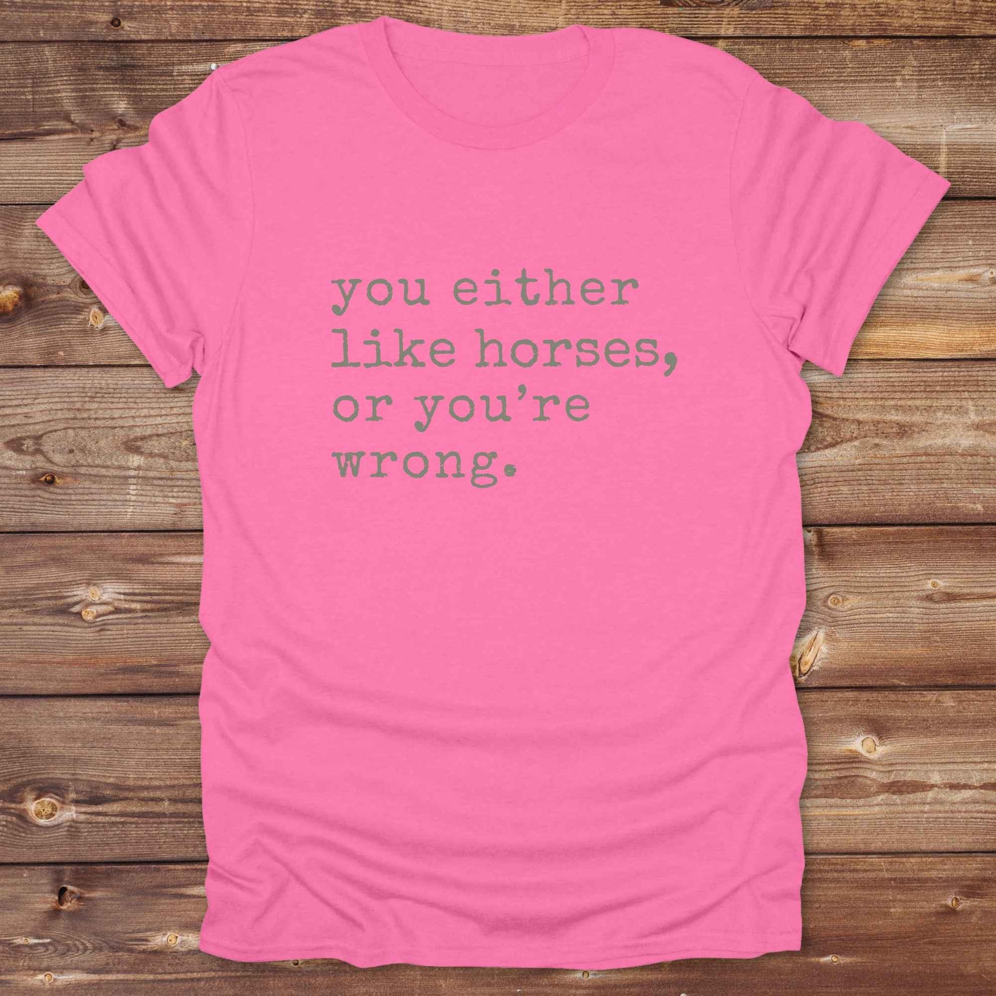 Pink t-shirt with text 'you either like horses, or you're wrong.' on a wooden background. Show your love for horses loud and proud with this funny typography western tee ,perfect for cowgirls, ranchers, and equestrians. 
This “You either like horses or you're wrong” t-shirt is a hilarious must have for horse lovers with sass and sarcasm. Ideal gift for any horse girl or cowboy, this rustic western Gildan tee blends humor with horse life perfectly. Whether you’re mucking stalls or riding trails, this sarcast
