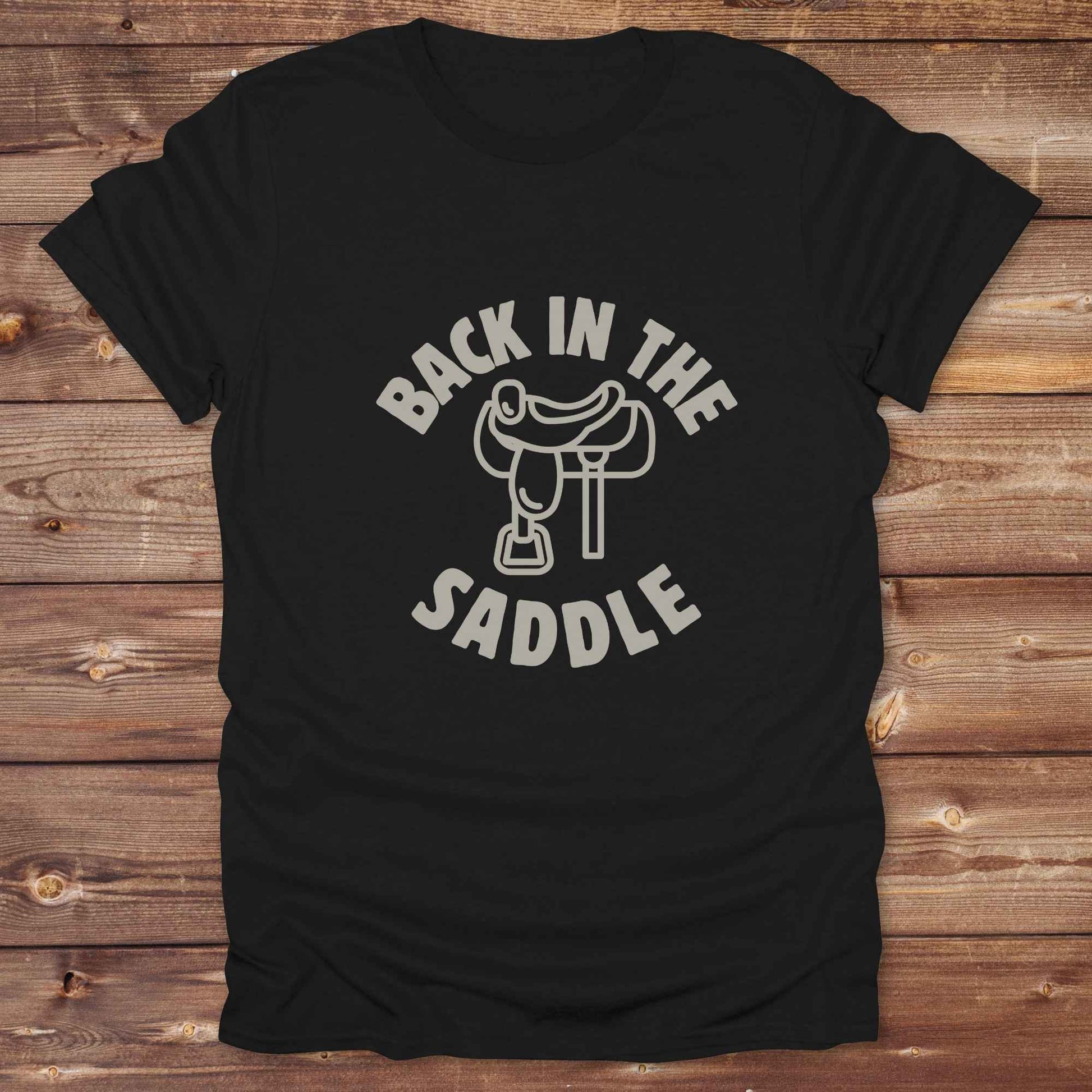 Our "Back in the Saddle" t-shirt is the perfect western-style graphic tee for cowboys and cowgirls who love horseback riding, rodeo culture, and rustic country fashion. Featuring a clean saddle illustration and retro western typography, this shirt blends comfort and character, making it ideal for ranch wear, horse lovers, and rodeo enthusiasts. Whether you're heading to a country concert, festival, or barn, this tee stands out. Makes a great gift for horse riders, western fans or anyone getting back riding