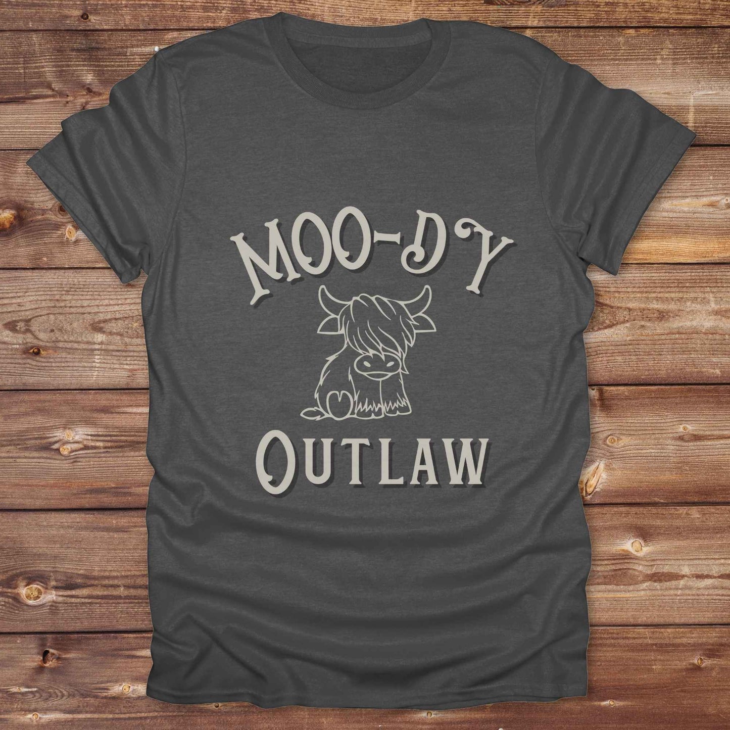 Meet the “Moo-Dy Outlaw” tee from Lasso and Loom a perfect mix of western sass and farmyard fun. Featuring a hand drawn moody Highland cow and outlaw typography, this western graphic tee is made for cowgirls, cowboys, and everyone who rides through life with a little attitude. It's ideal for rodeos, ranch days, and social media selfies with rustic vibes and comfort in every stitch. Whether you're shopping for yourself or gifting a cow lover with a sense of humor, this shirt is guaranteed to wrangle smiles