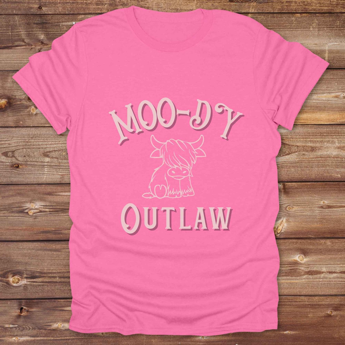 Meet the “Moo-Dy Outlaw” tee from Lasso and Loom a perfect mix of western sass and farmyard fun. Featuring a hand drawn moody Highland cow and outlaw typography, this western graphic tee is made for cowgirls, cowboys, and everyone who rides through life with a little attitude. It's ideal for rodeos, ranch days, and social media selfies with rustic vibes and comfort in every stitch. Whether you're shopping for yourself or gifting a cow lover with a sense of humor, this shirt is guaranteed to wrangle smiles
