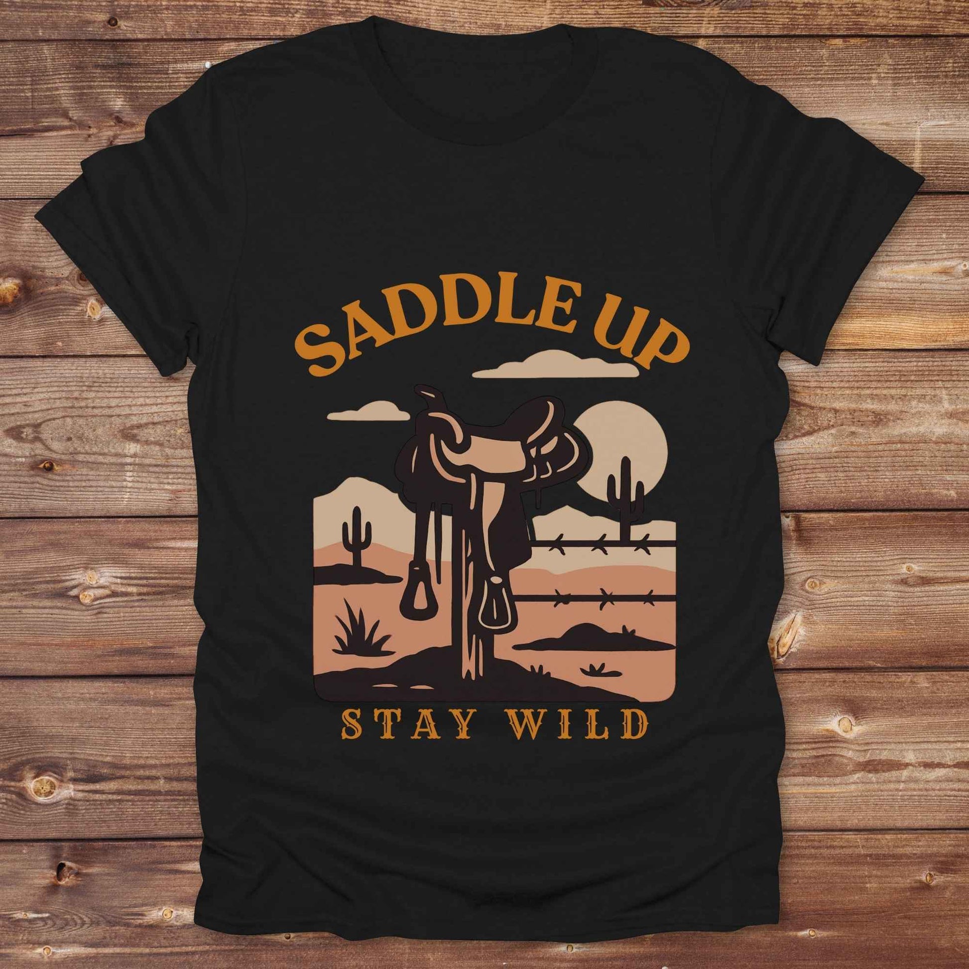 Saddle Up Stay Wild western t-shirt features a bold desert sunset graphic with a classic saddle and western landscape. Perfect for cowgirls, cowboys, and horse lovers, this rustic tee blends adventure with comfort and country charm. Whether you're heading to a rodeo, trail ride, or simply embracing your wild side, this shirt offers a soft fit and bold design. Designed for western wear fans, equestrians, and country souls, it's a must have for anyone who lives the saddle life.