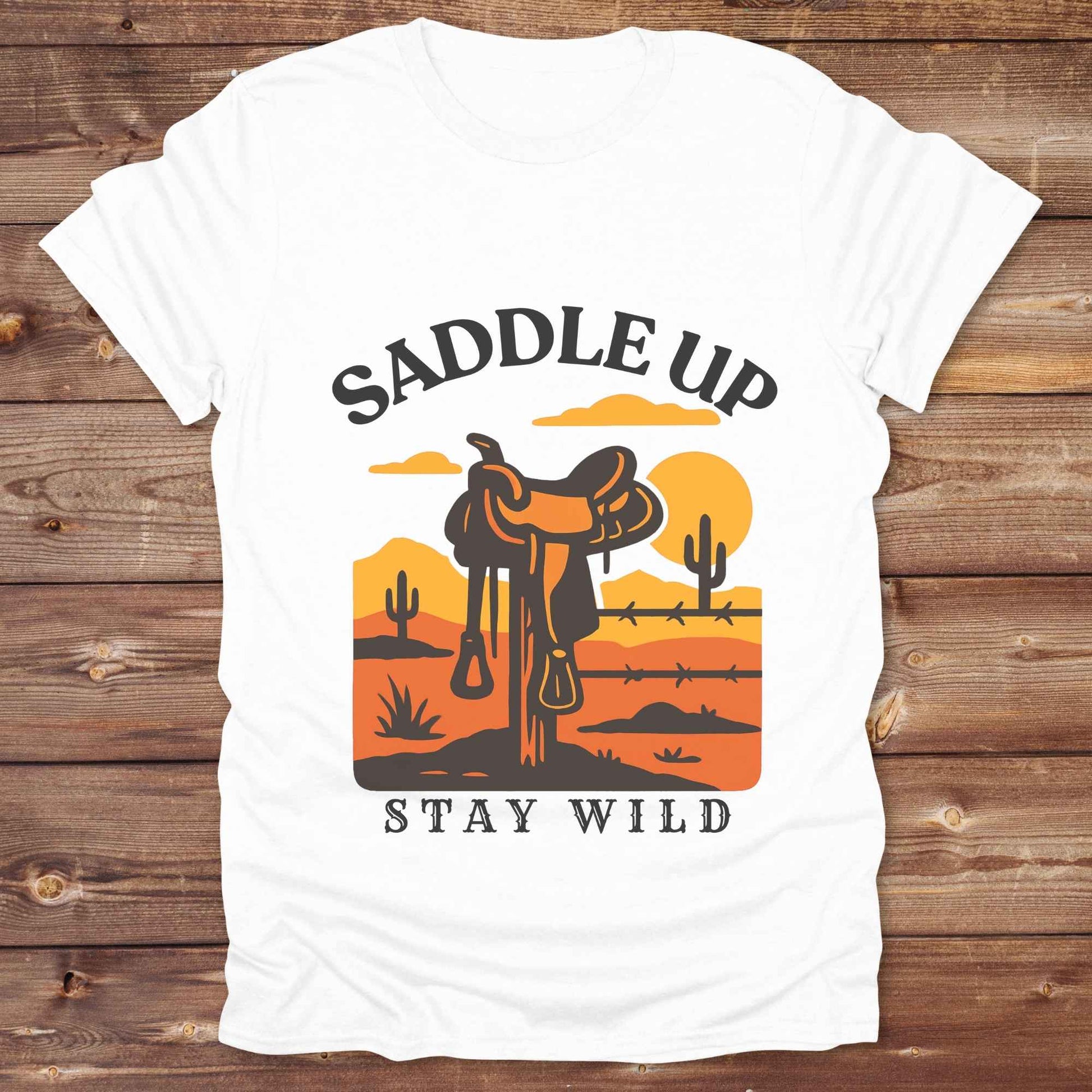 Saddle Up Stay Wild western t-shirt features a bold desert sunset graphic with a classic saddle and western landscape. Perfect for cowgirls, cowboys, and horse lovers, this rustic tee blends adventure with comfort and country charm. Whether you're heading to a rodeo, trail ride, or simply embracing your wild side, this shirt offers a soft fit and bold design. Designed for western wear fans, equestrians, and country souls, it's a must have for anyone who lives the saddle life.