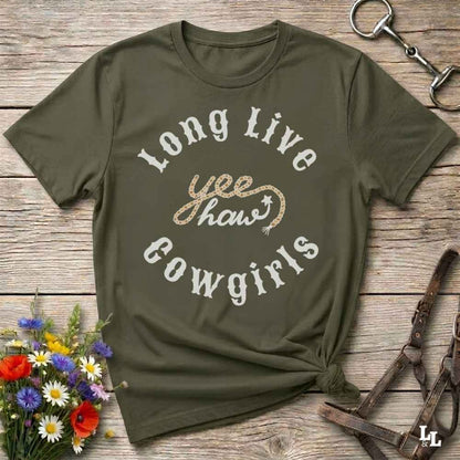 An olive green graphic t-shirt with the text 'Long Live yee haw!' in white and glittery gold, styled in a flat-lay on a rustic wooden background with equestrian accessories and flowers.