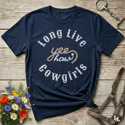 A navy blue graphic t-shirt with 'Long Live yee haws cowgirls' printed on the front, styled in a flat-lay on a rustic wooden background with equestrian accessories and flowers.