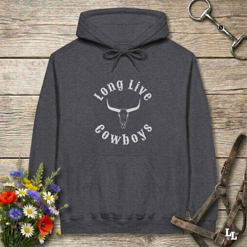 A dark heather gray hoodie with a white graphic reading 'Long Live Cowboys' around a steer skull, laid flat on a rustic wood plank background with flowers and horse tack props.