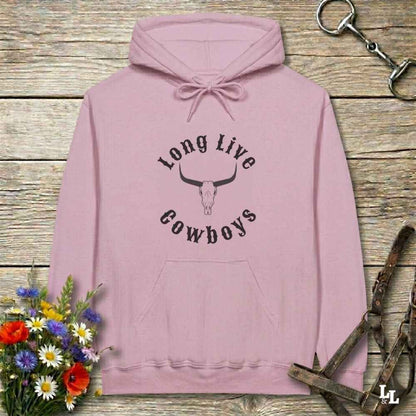 A dusty pink pullover hoodie with a black graphic print reading 'Long Live Cowboys' around a longhorn skull, laid flat on a rustic wooden surface with decorative flowers and horse tack props.