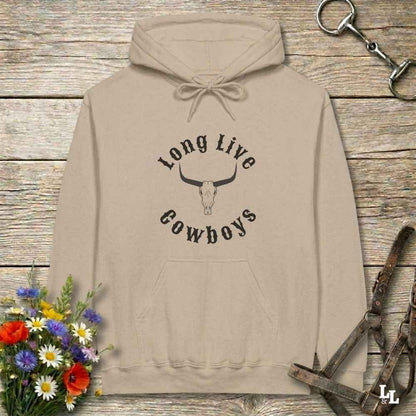 A beige pullover hoodie with a black graphic reading 'Long Live Cowboys' around a longhorn skull, laid flat on a rustic wood surface with flowers and horse tack props around it.