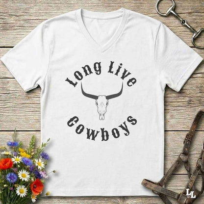 A white V-neck t-shirt with a black graphic reading 'Long Live Cowboys' around a longhorn skull, laid flat on a rustic wooden surface with flowers and horse tack props.