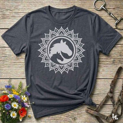 A dark heather gray t-shirt with a white horse head mandala graphic, styled in a flat-lay on a rustic wooden background with equestrian accessories and flowers.