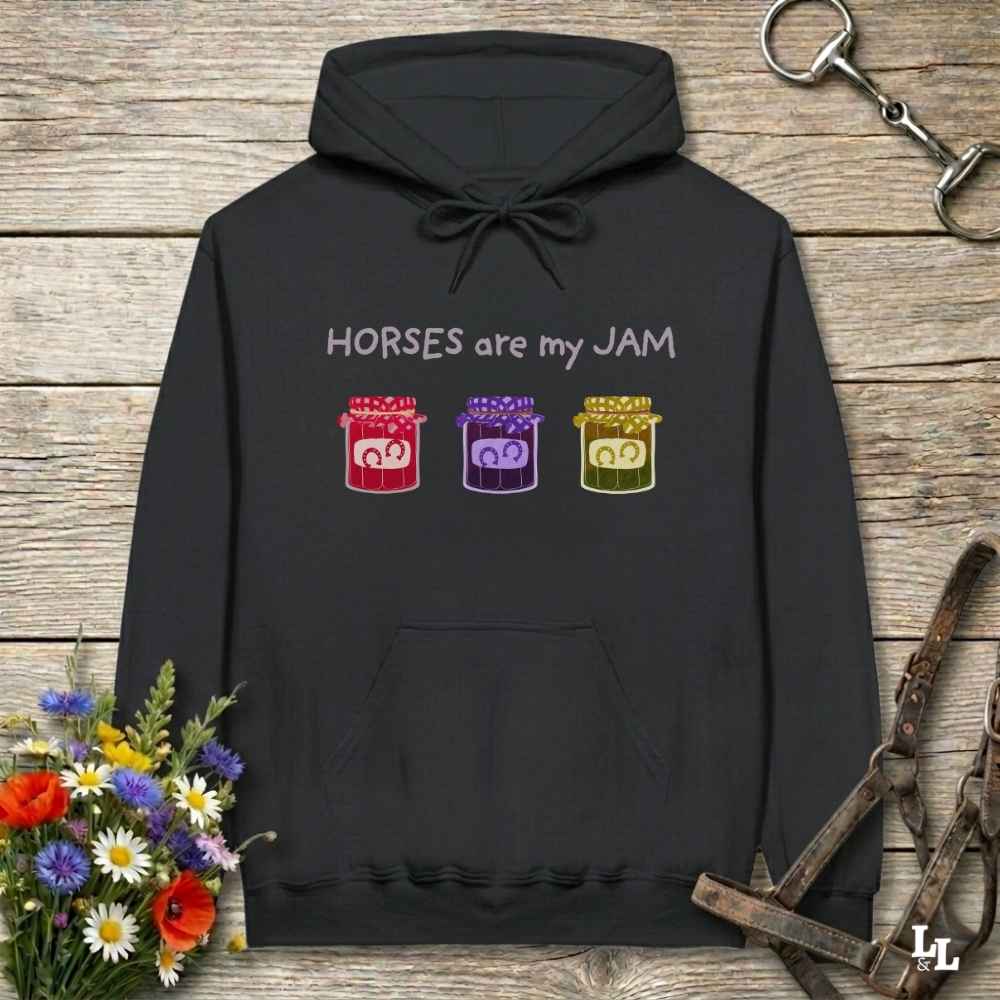 Black hoodie with 'Horses are my JAM' text and jelly jar graphics on a wooden surface with floral and equestrian equipment.