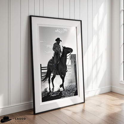 Framed black and white artwork of a cowboy on horseback in a room with wooden flooring and white walls.