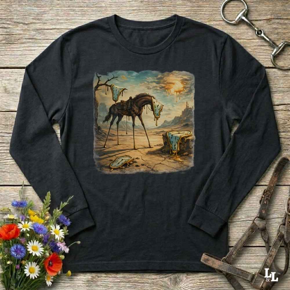 A black long-sleeve t-shirt with a vintage-style western illustration of a broken horse on a cracked desert landscape, displayed on a rustic wooden background with horse tack and flowers.