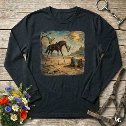 A black long-sleeve t-shirt with a vintage-style western illustration of a broken horse on a cracked desert landscape, displayed on a rustic wooden background with horse tack and flowers.
