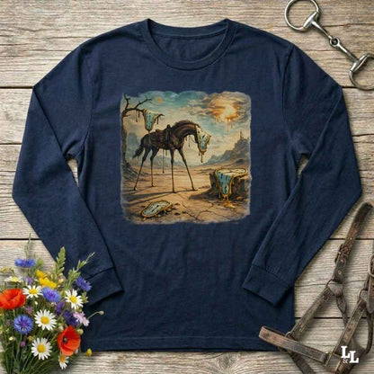 A navy blue long-sleeve t-shirt with a vintage western-style graphic print of a horse standing in a desert landscape. The shirt is displayed flat on a rustic wooden background, styled with equestrian accessories (a horse bit in the top right and a halter in the bottom right) and a small bouquet of colorful wildflowers in the bottom left.