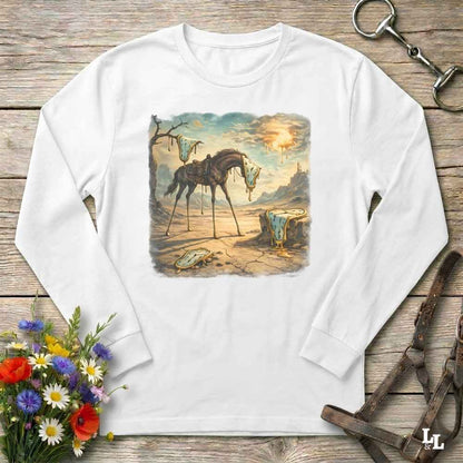 A white long-sleeve t-shirt with a vintage-style graphic print of a skeletal horse in a desert landscape, displayed flat on a rustic wooden background with equestrian accessories and flowers.