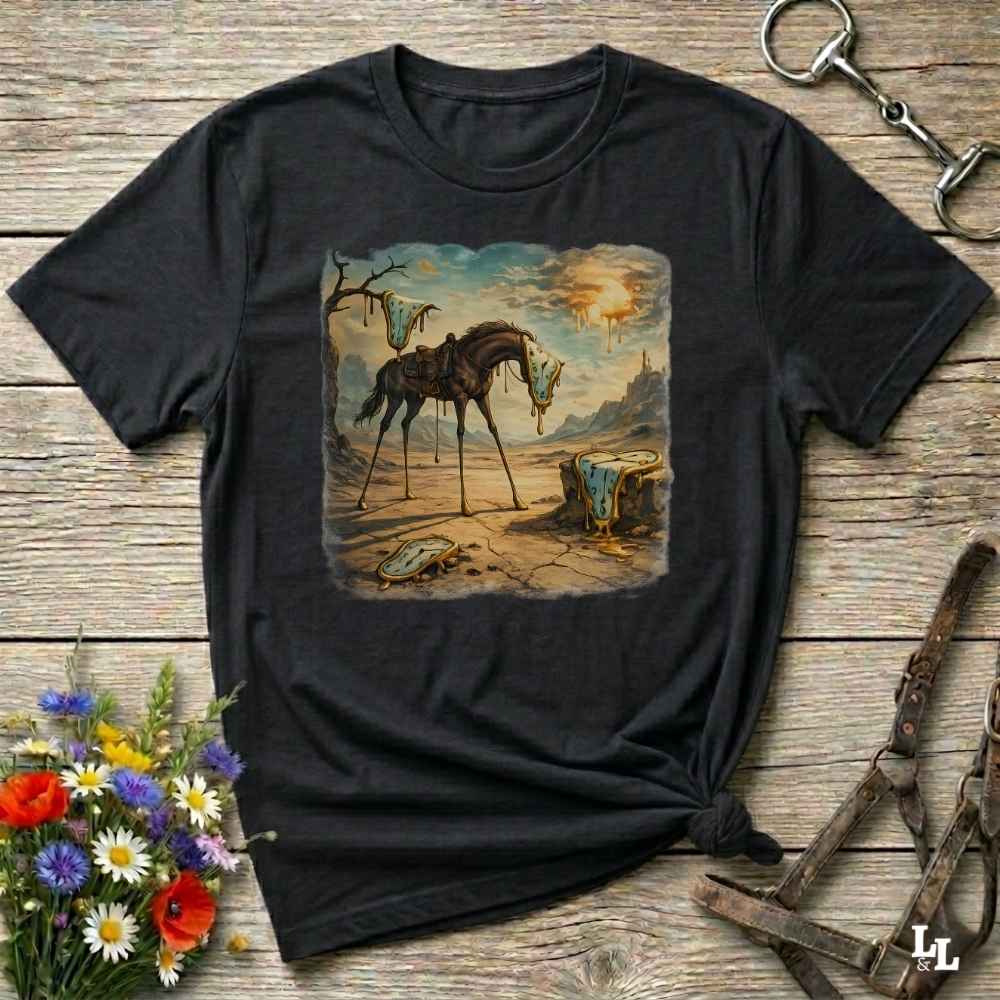 A black graphic t-shirt laid flat on a rustic wooden surface, styled with equestrian accessories and a small bouquet of flowers. The t-shirt features a square vintage-style illustration of a skeletal horse standing in a barren landscape.