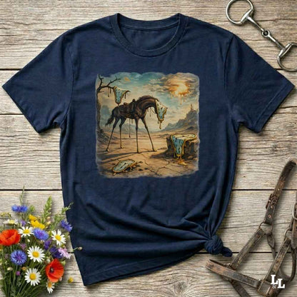 A navy blue graphic t-shirt laid flat on a rustic wooden surface, styled with equestrian accessories and a small bouquet of flowers. The t-shirt features a square vintage-style illustration of a skeletal horse standing in a barren landscape.