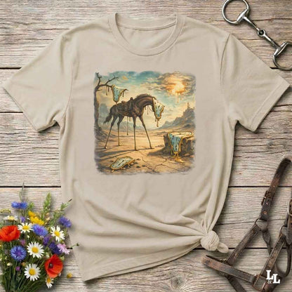 A beige graphic t-shirt with a vintage-style illustration of a horse in a desert landscape, styled in a flat-lay on a rustic wooden background with equestrian accessories and flowers.