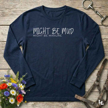 A navy blue long-sleeve t-shirt with white printed text reading 'MIGHT BE MUD' and 'MIGHT BE MANURE' on the chest, laid flat on a rustic wooden background with decorative flowers and horse tack around it.