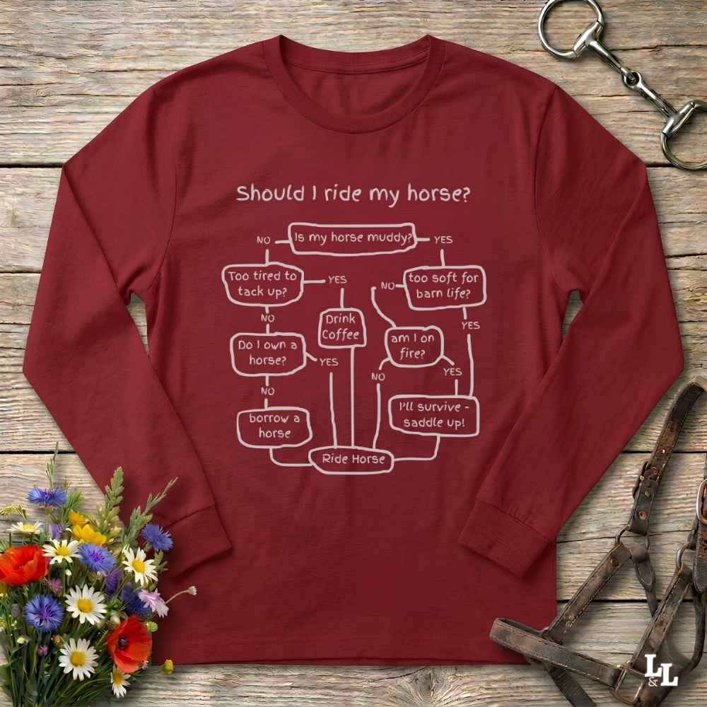 A long-sleeve maroon t-shirt with a white printed flowchart graphic titled 'Should I ride my horse?' laid flat on a rustic wooden surface. The shirt is styled with equestrian accessories (a leather bridle) and a small bouquet of wildflowers.