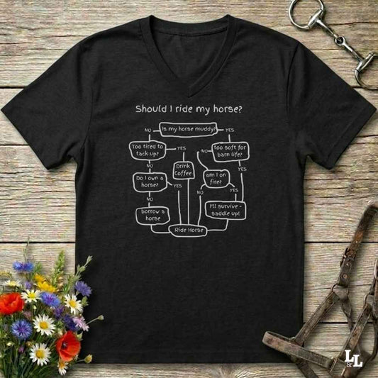 A black V-neck t-shirt with a white printed flowchart titled 'Should I ride my horse?' laid flat on a rustic wooden surface. The shirt is styled with a horse bridle, a horse bit, and a small bouquet of wildflowers.