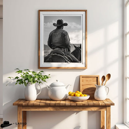 Framed black and white photo of a cowboy on a wall above a wooden table with a teapot, lemons, and a plant.