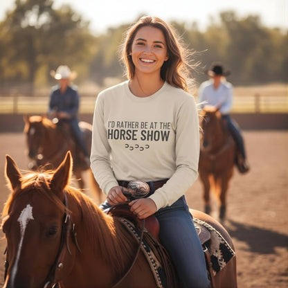Woman riding a horse with a shirt that says 'I'd rather be at the horse show' in an outdoor equestrian setting.  I'd Rather be at the Horse Show Long Sleeve Tee for Horse Lovers, Trail Riding Tee, ideal for a gift