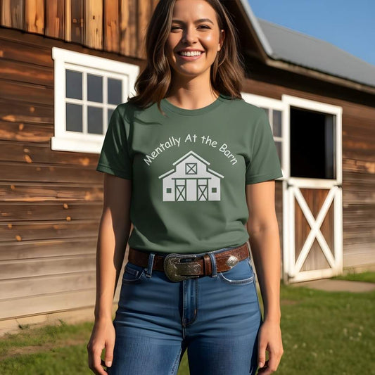 Woman wearing a green t-shirt with a barn graphic in front of a wooden . Mentally at the Barn T-Shirt for Horse Lovers, Riding Tee Barn Wear Teebuilding.
