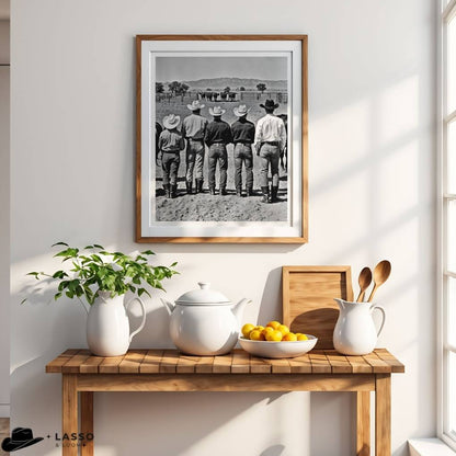 Framed black and white photo of cowboys on a wall above a wooden table with a teapot, lemons, and a plant.