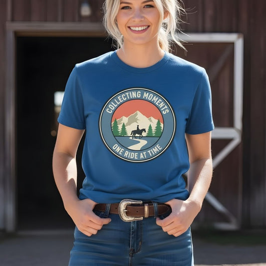 Woman wearing a blue t-shirt with a graphic design and text, standing in front of a wooden building. Collecting Moments One Ride at a Time T-Shirt for Horse Lovers, Horse Riding Tee