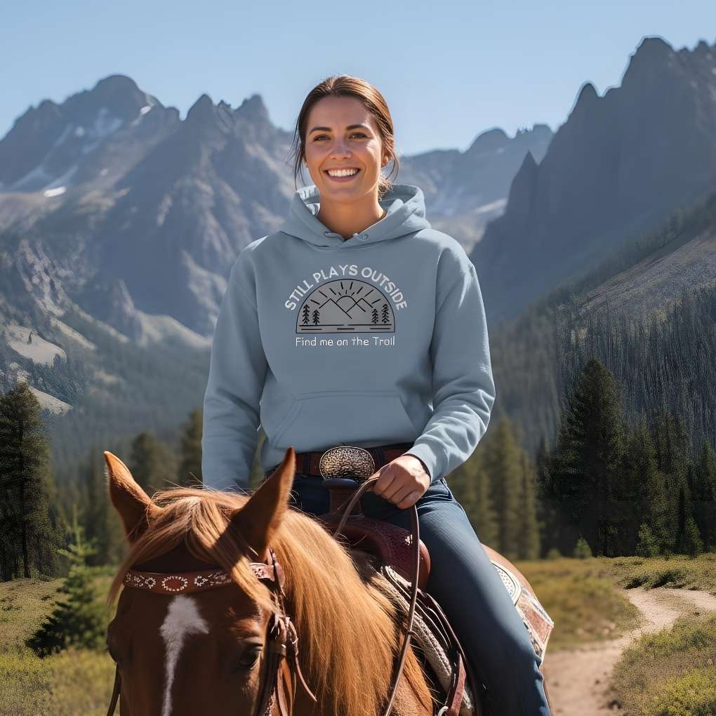 Woman riding a horse with mountains in the background wearing a hoodie with text and graphics. Still Plays Outside Hoodie for Horse Lovers, Cozy Barn Wear Horse Riding Hoodie