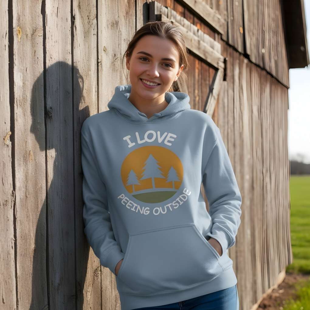 Woman wearing a light blue hoodie with a nature-themed design, standing against a wooden wall. I Love Peeing Outside Hoodie for Horse Riders, Cozy Barn Wear Hoodie, Equestrian Apparel