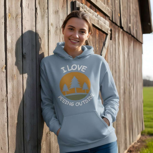 Woman wearing a light blue hoodie with a nature-themed design, standing against a wooden wall. I Love Peeing Outside Hoodie for Horse Riders, Cozy Barn Wear Hoodie, Equestrian Apparel