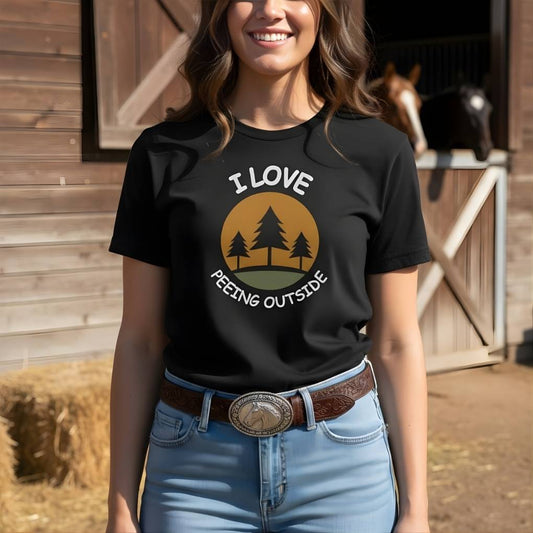 Person wearing a black t-shirt with 'I LOVE PEEING OUTSIDE' design in front of a wooden building. I Love Peeing Outside T-Shirt for Horse Lovers, Trail Riding Tee, Horse Rider Tee