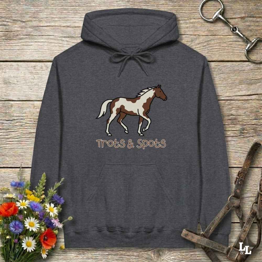 Gray hoodie with horse design and 'Trots & Spots' text on a wooden surface with floral and equestrian accessories.