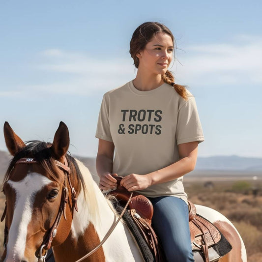 Woman riding a horse wearing a t-shirt with 'TROTS & SPOTS' text in a desert setting. Trots and Spots T-Shirt for Pinto Horse Lover, Trail Riding Tee for Horse Rider
